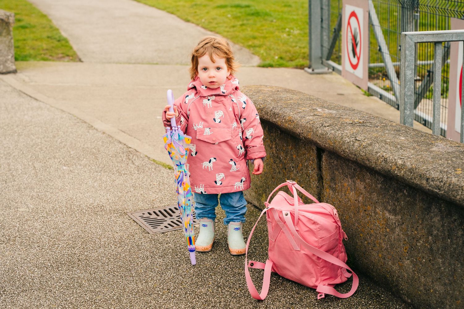 A child plays outside with a pink wheeled toy on a paved walkway near a grassy area. PHOTOGRAPHER Dublin