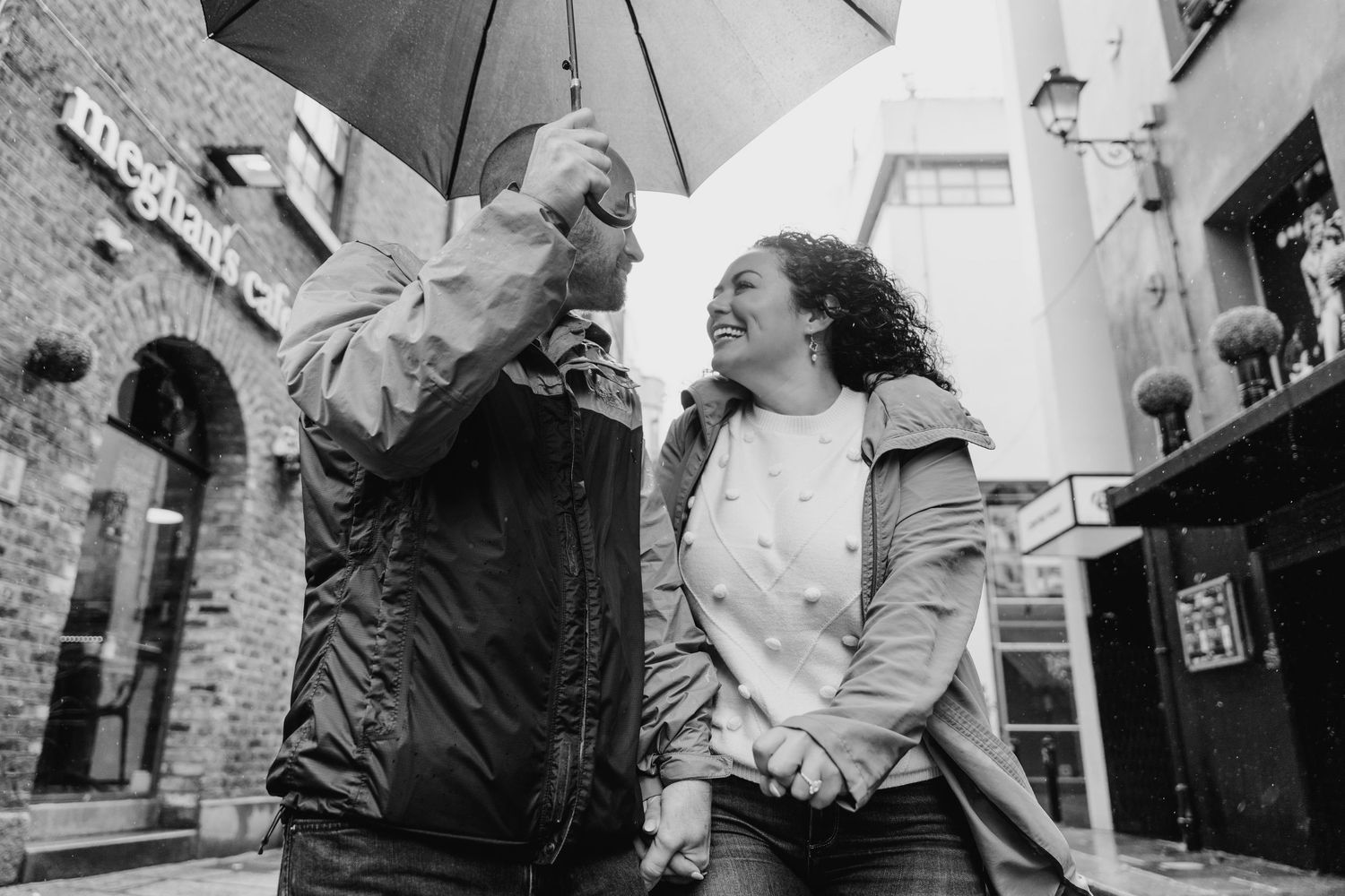 Black and white photo series captures intimate moments between a couple walking with umbrellas in an urban setting. Proposal Dublin Photogra