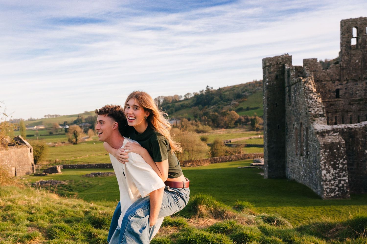 Two people playing and laughing together near ancient castle ruins in a green countryside setting. Photographer Ireland dublin