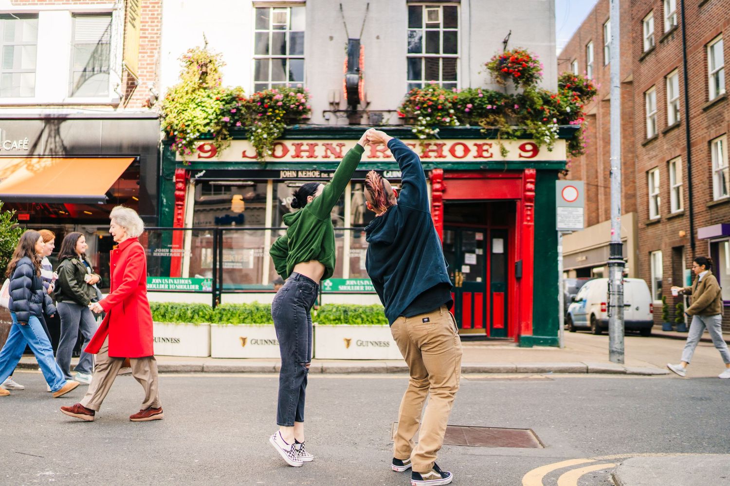 Three people interact on a city street outside a traditional pub with hanging flower baskets. PHOTOGRAPHER Dublin Ireland