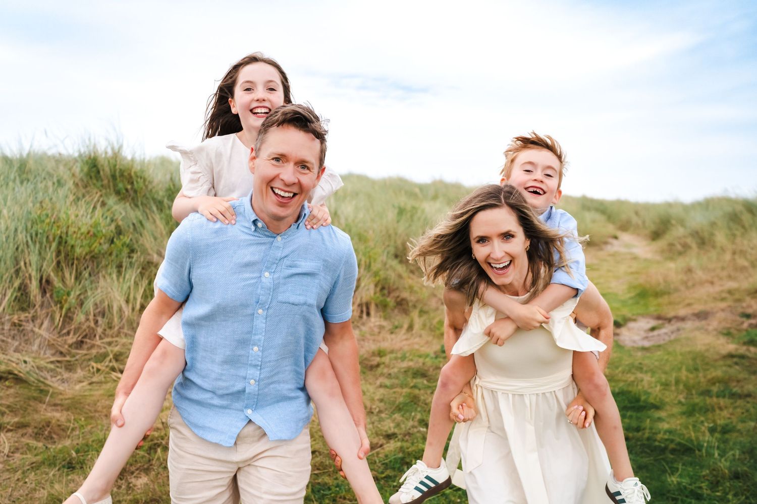 Family having fun and laughing together on coastal sand dunes during golden hour.  Family photographer Dublin Ireland