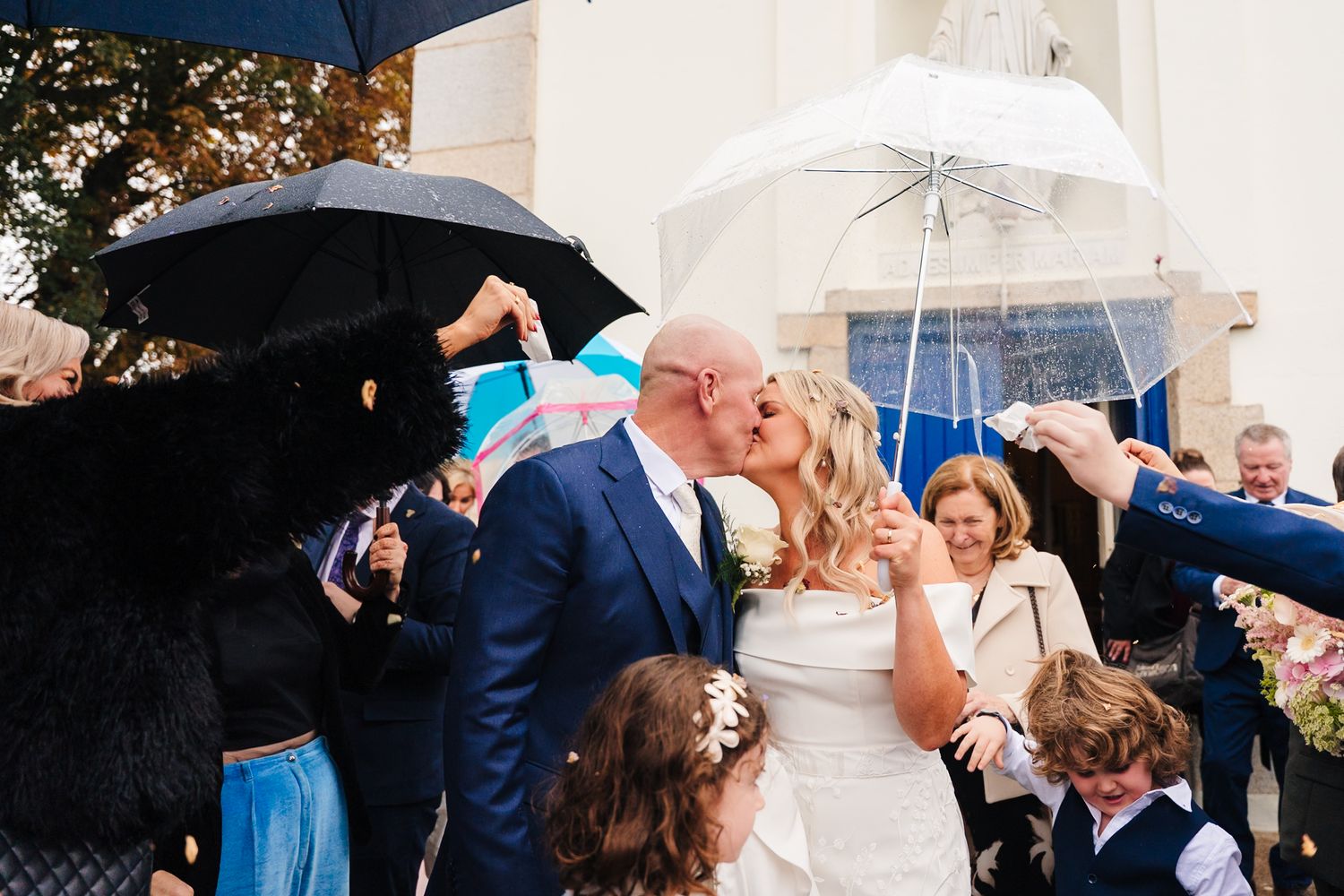 Wedding party gathers under umbrellas during rainy outdoor ceremony. The Dean Dublin Wedding Photographer