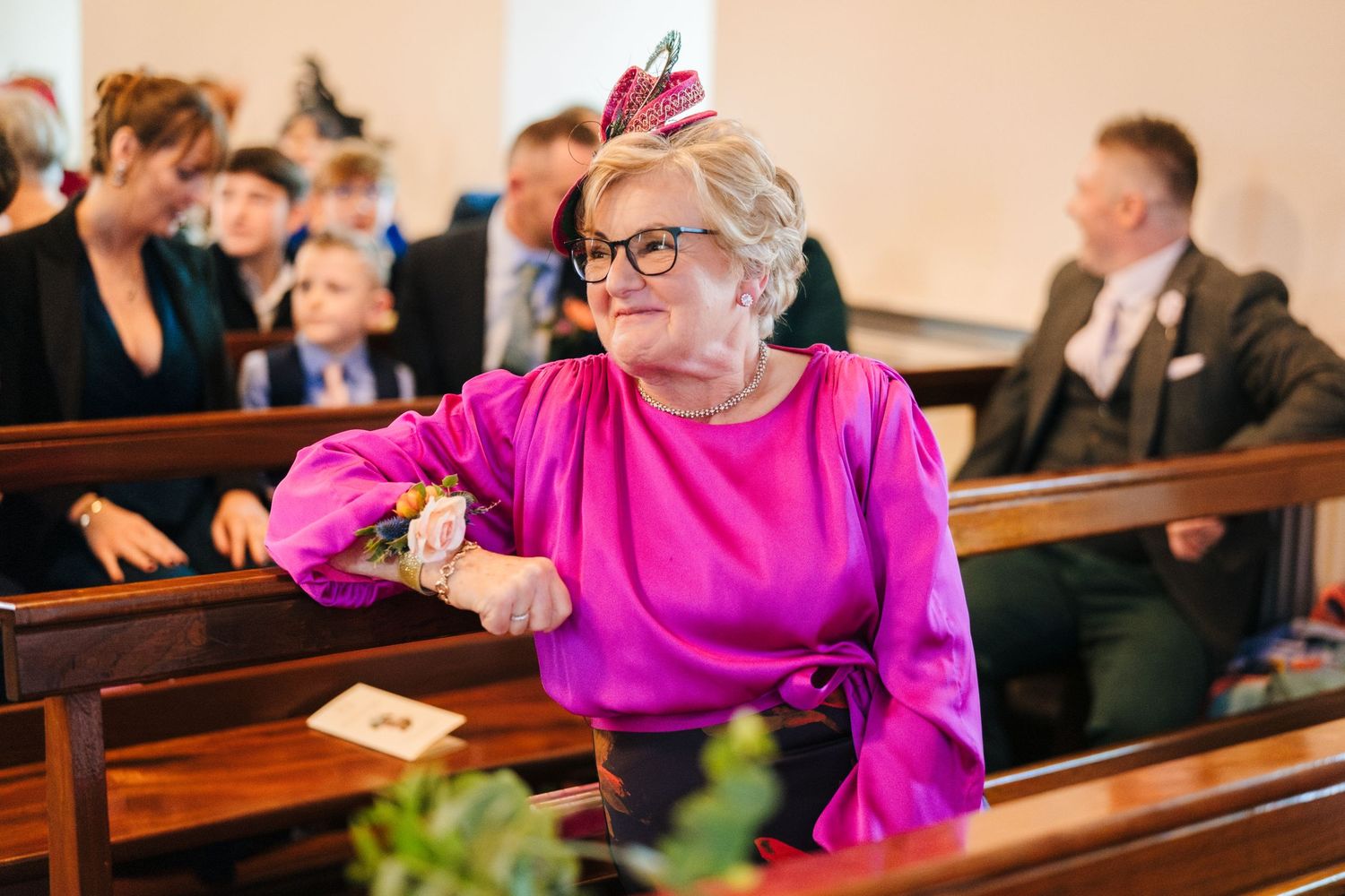 Wedding guests in bright pink attire seated in wooden church pews during ceremony.