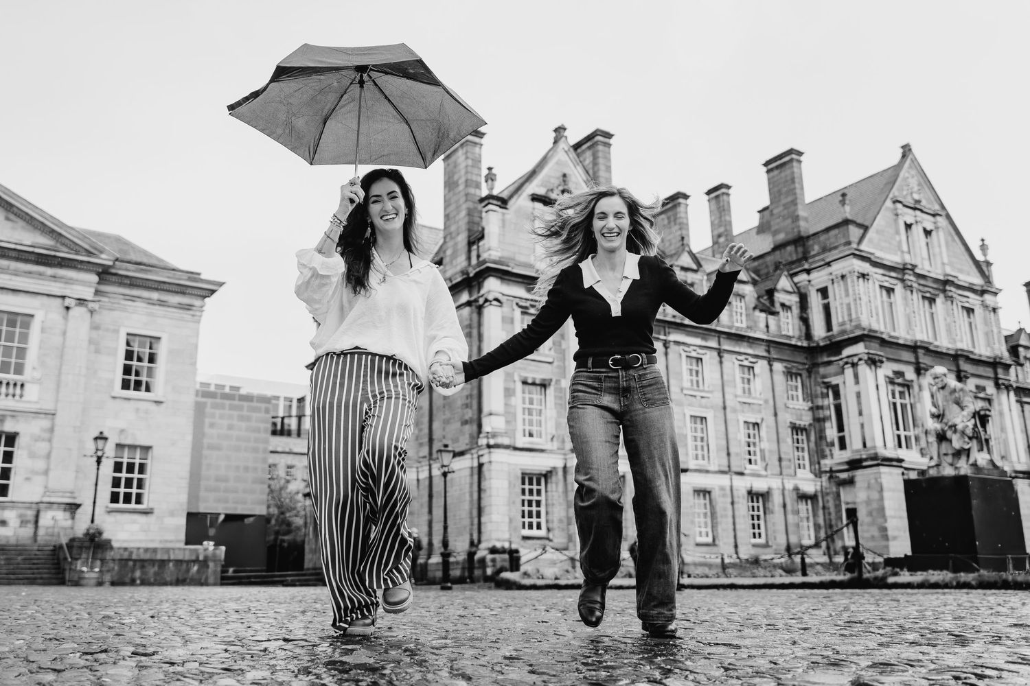 Black and white photo of people walking with umbrellas near historic buildings. professional headshots dublin photographer