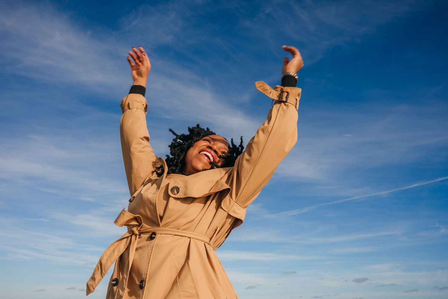 Figure in beige coat dancing joyfully against vibrant blue sky. Dublin professional headshot photographer
