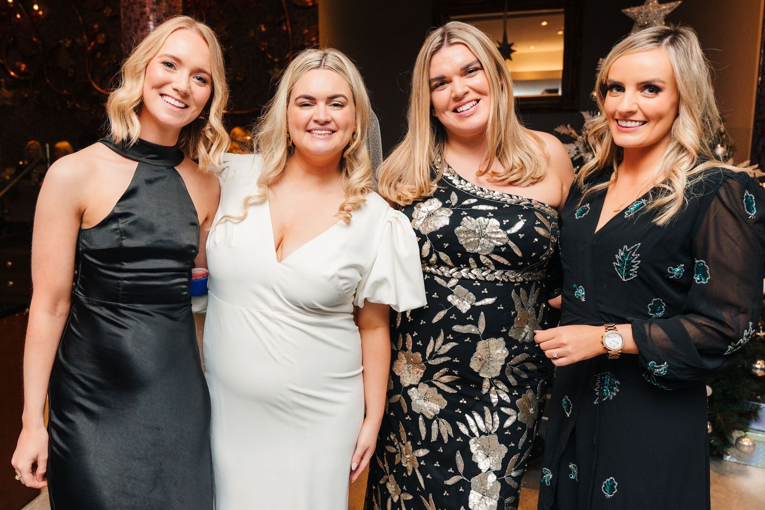 Wedding celebration group photo with attendees in formal black and white attire at an indoor venue. Wedding photographer dublin
