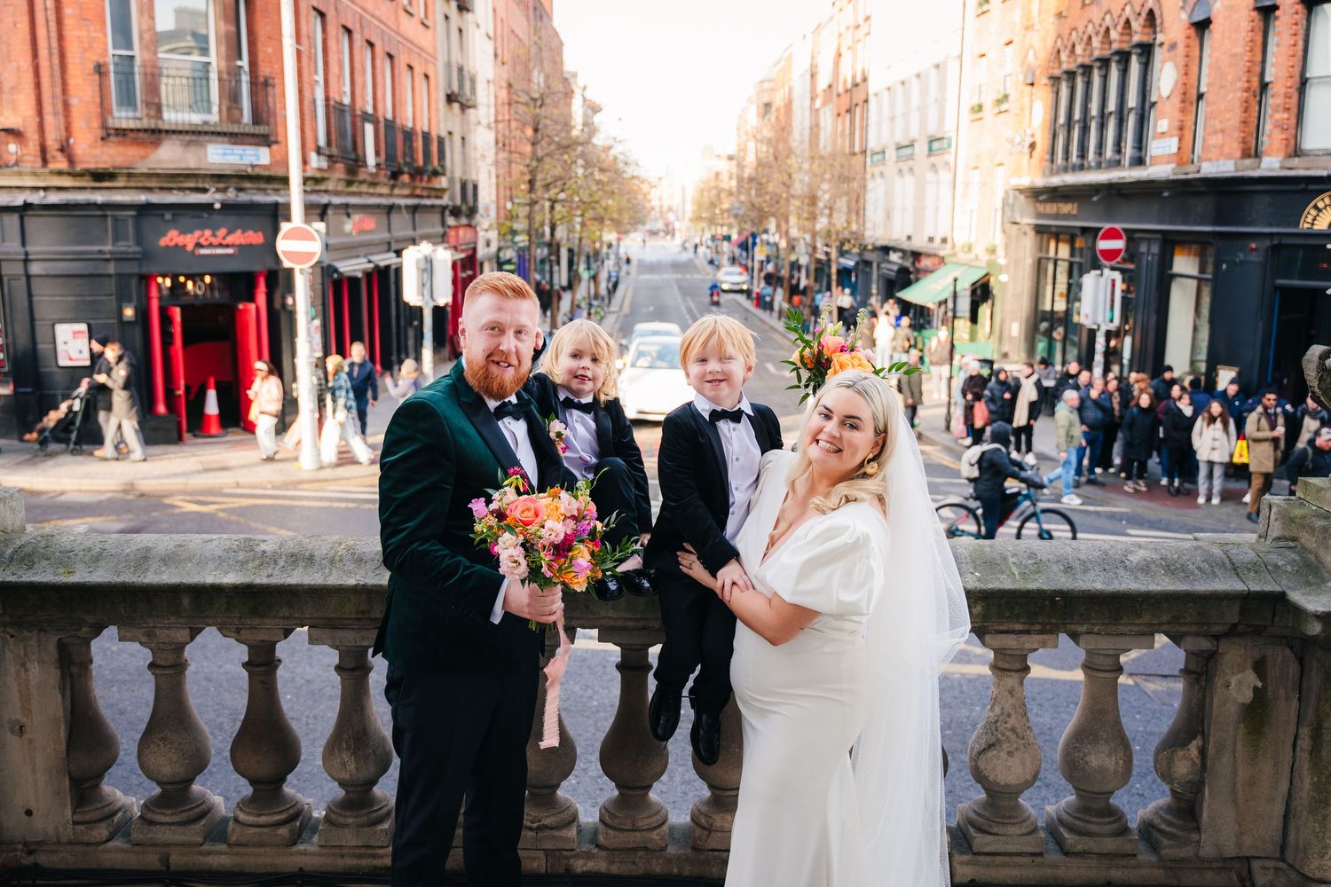 Wedding party poses on city streets with historic brick buildings in background. Wedding photographer dublin