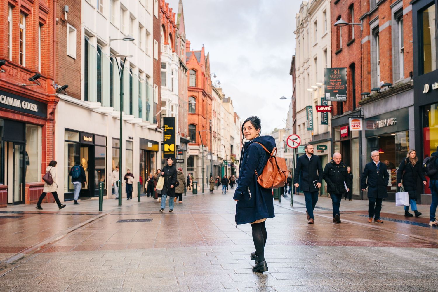 People walking down a historic brick-paved shopping street in Dublin's city center on a cloudy day. professional headshots dublin