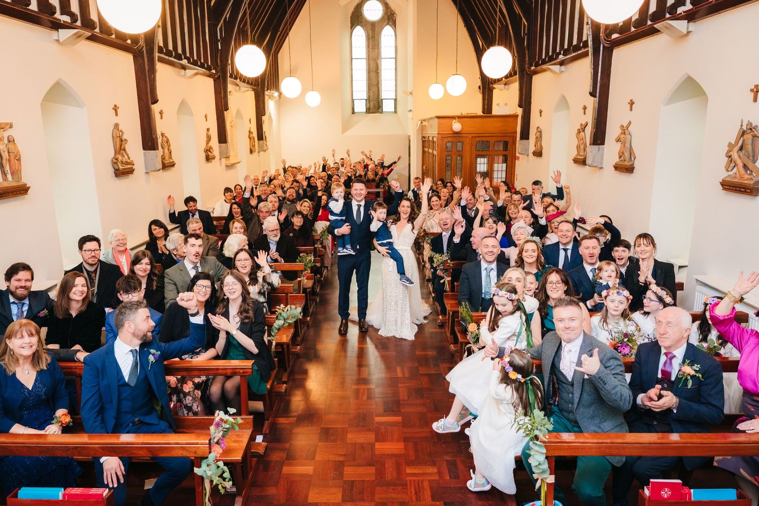 Wedding guests fill church pews during ceremony in historic chapel with wooden beams.