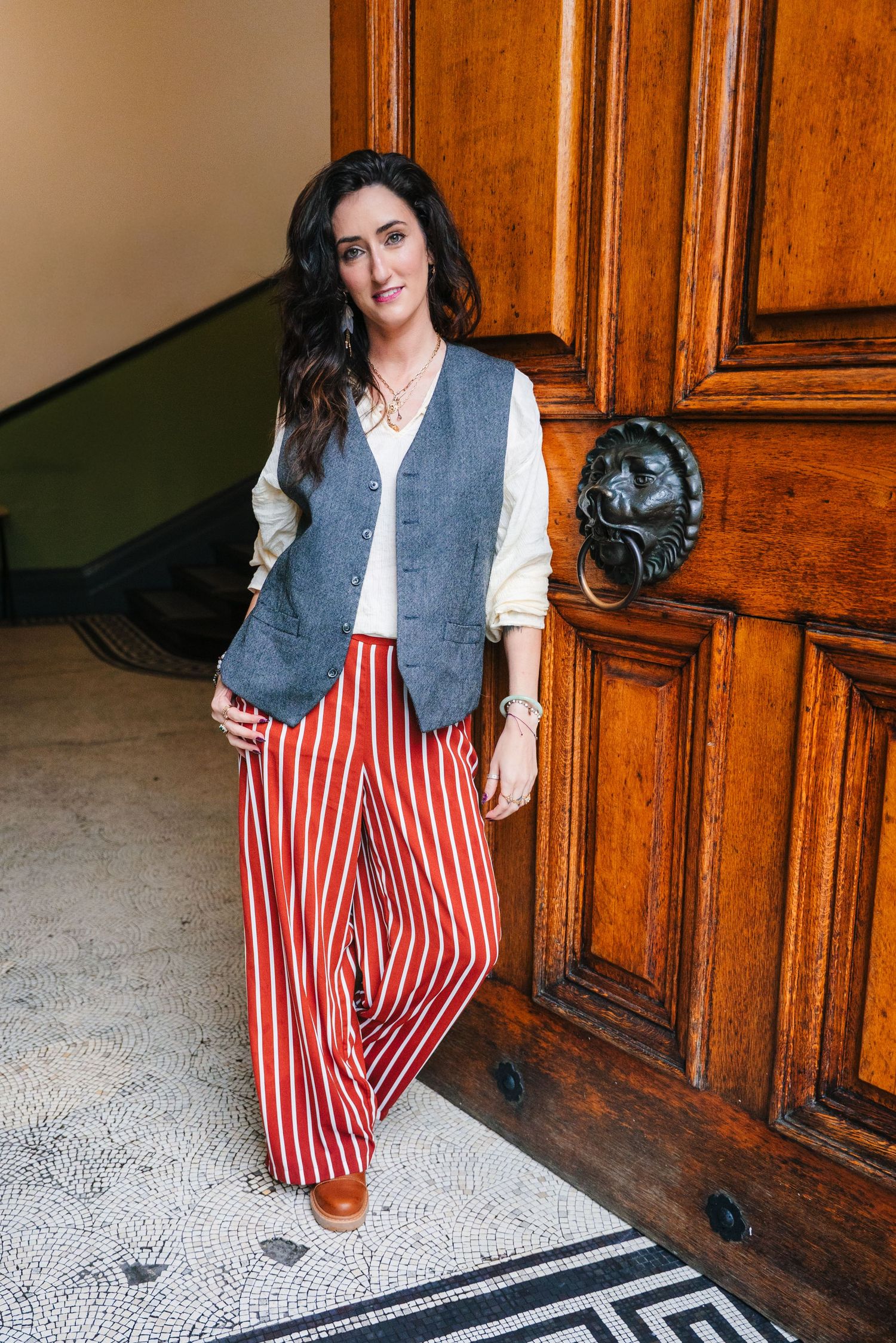 Indoor fashion shoot featuring gray vest, white blouse and red striped pants against wooden paneling. professional headshots dublin photogra