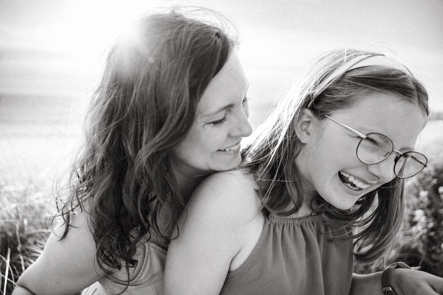 A candid black and white portrait of two young people sharing a joyful, laughing moment outdoors. family PHOTOGRAPHER Dublin