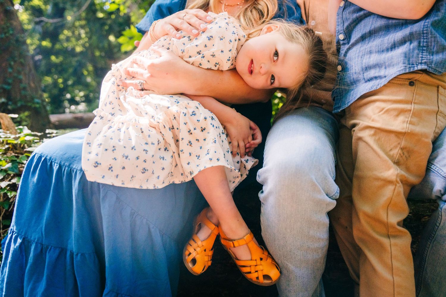 Small child in floral dress resting on blue dress with yellow shoes in outdoor garden setting. family PHOTOGRAPHER Dublin