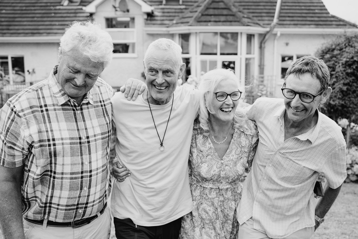 A black and white candid shot shows four people sharing a joyful moment together outdoors. family PHOTOGRAPHER Dublin