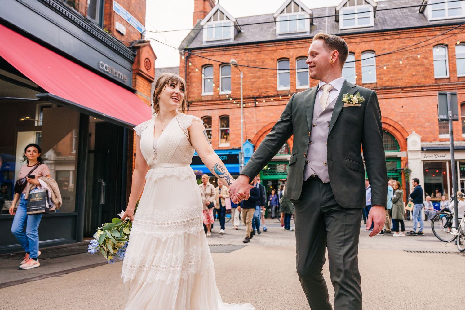 Newlyweds holding hands while walking through city street with historic architecture.PHOTOGRAPHER Dublin Ireland Wedding