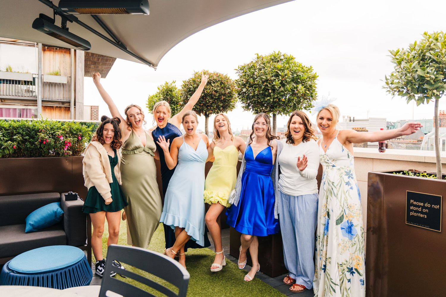Group of friends celebrating on a rooftop patio with drinks and summer dresses.PHOTOGRAPHER Dublin Ireland Wedding