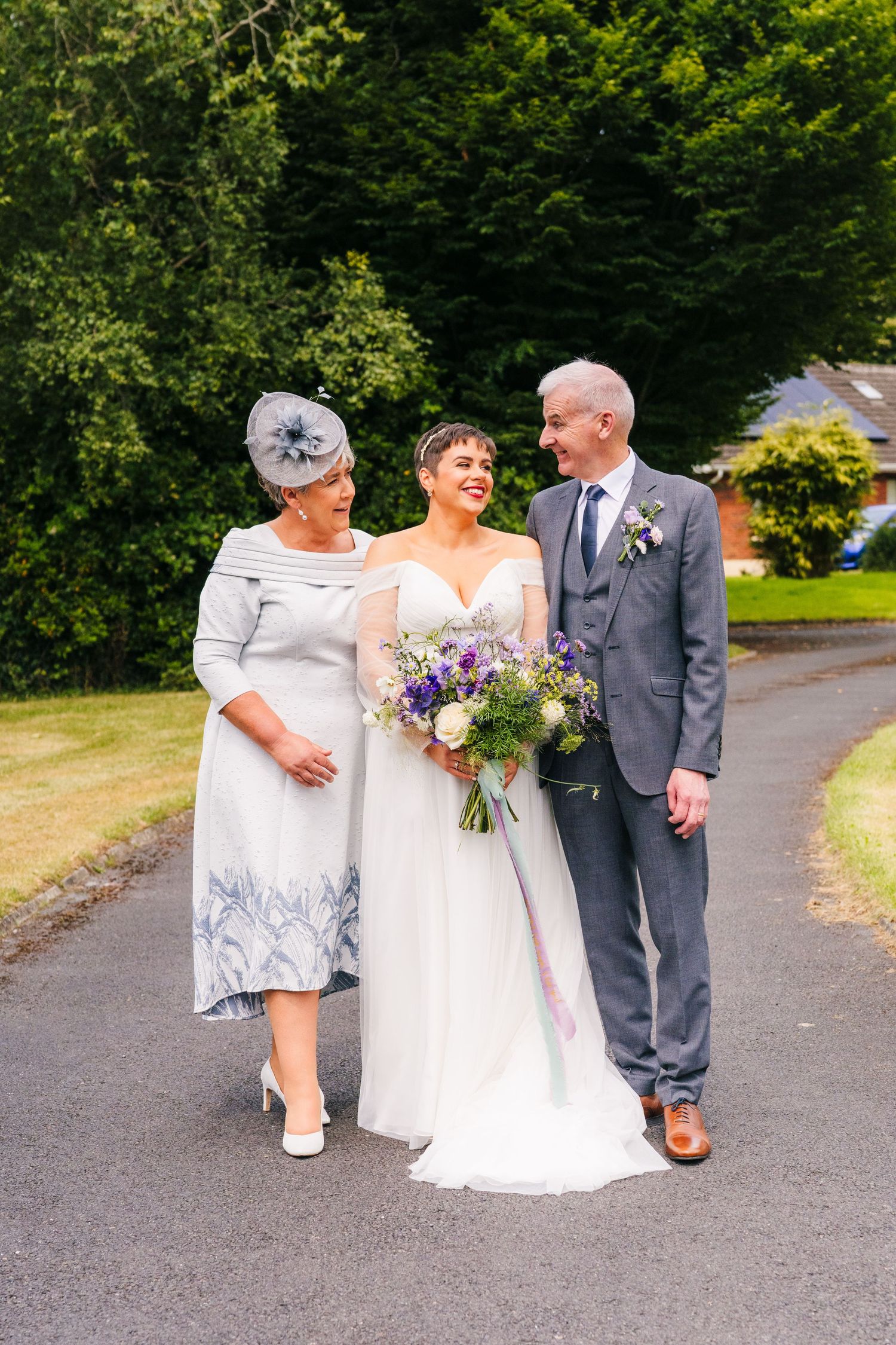 Millhouse slane wedding photographer dubliWedding party members walk together on a path while holding a beautiful purple and white bouquet.