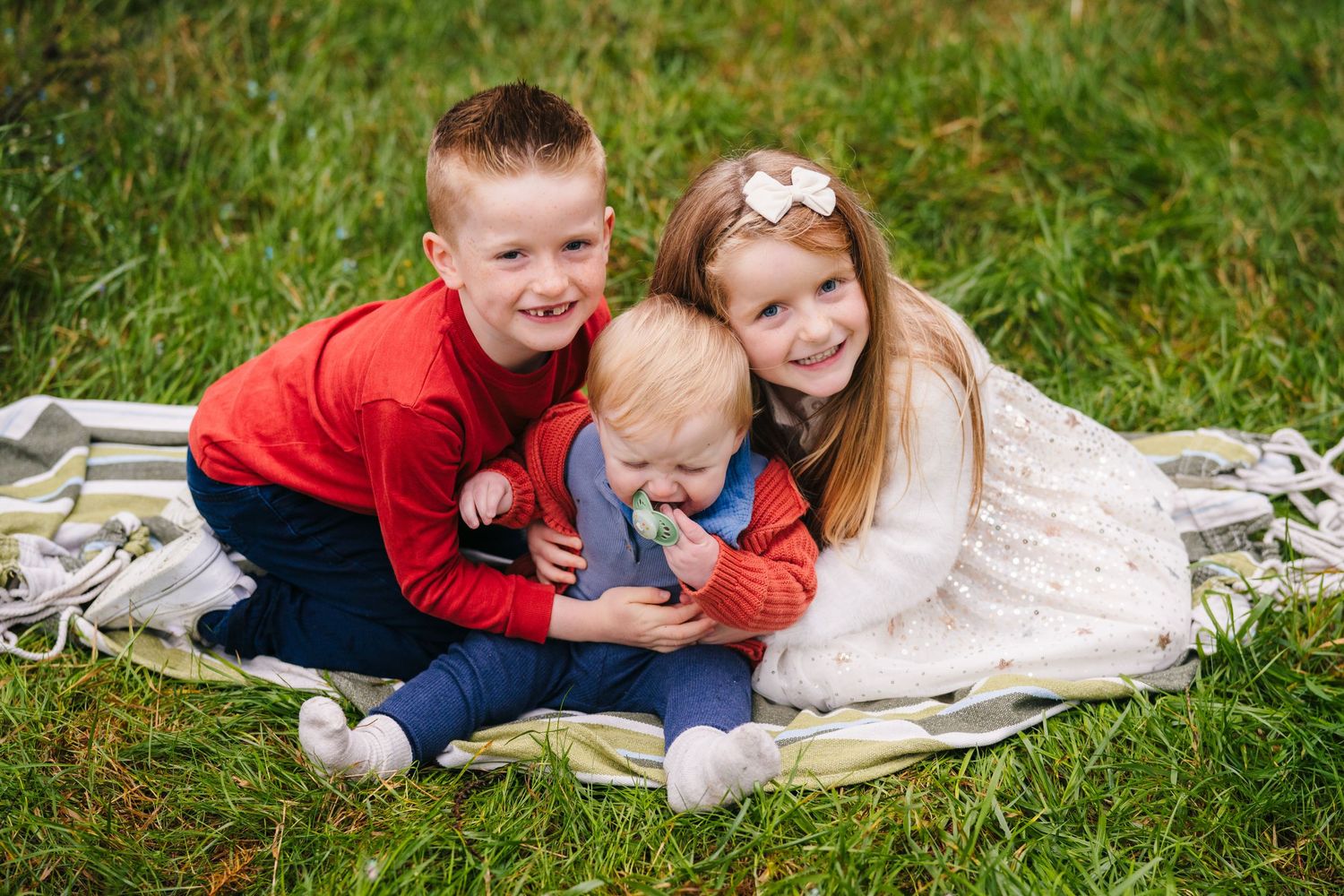 Three children sit together on blanket outdoors during autumn photoshoot.