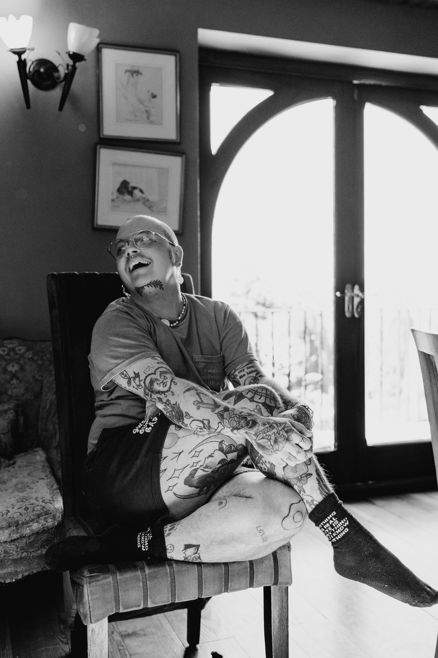 Poulaphouca Wedding photographer wicklowA black and white photo shows someone in casual attire relaxing on a chair beside an arched window.