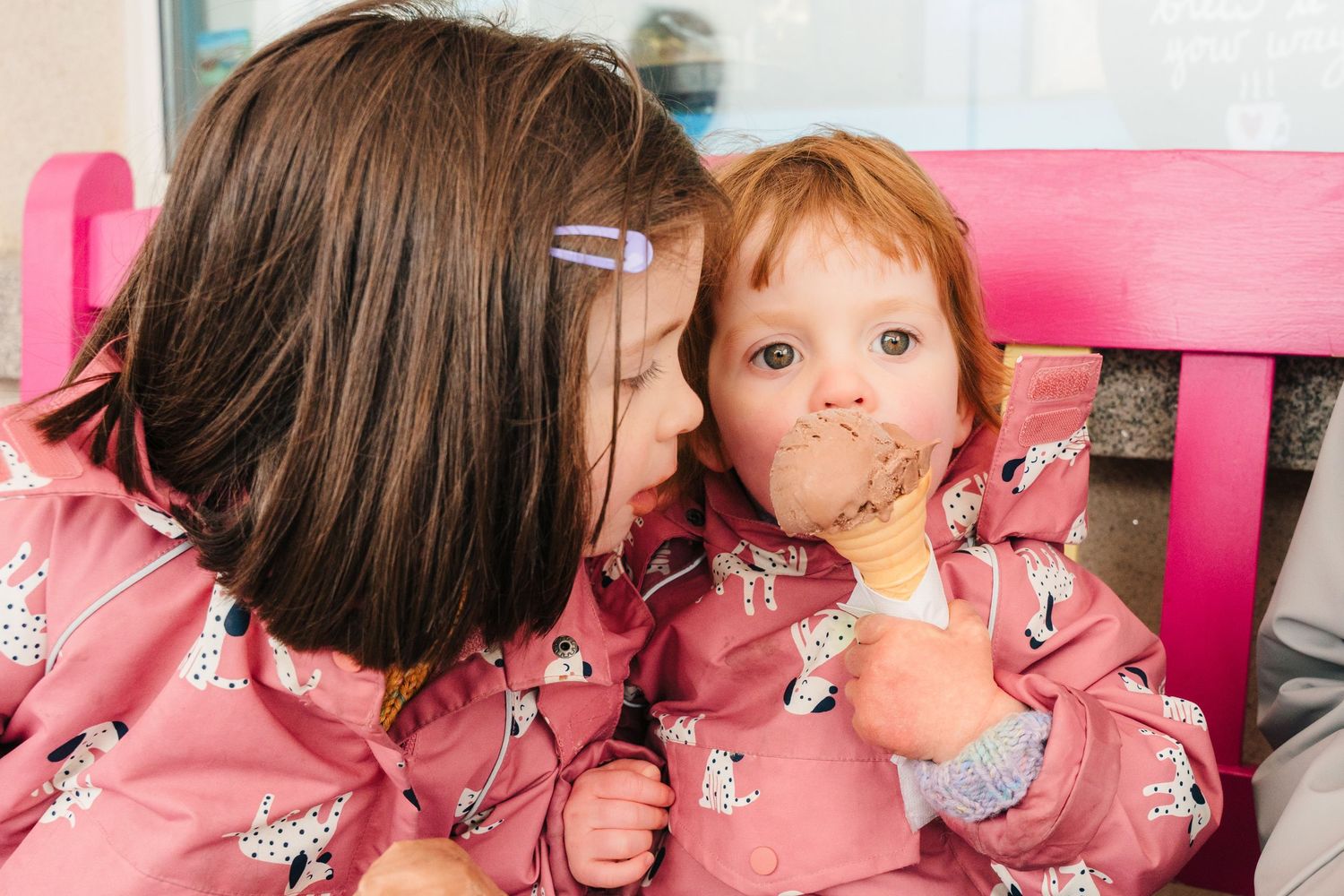 Two kids in matching pink outfits sharing ice cream cones. PHOTOGRAPHER Dublin