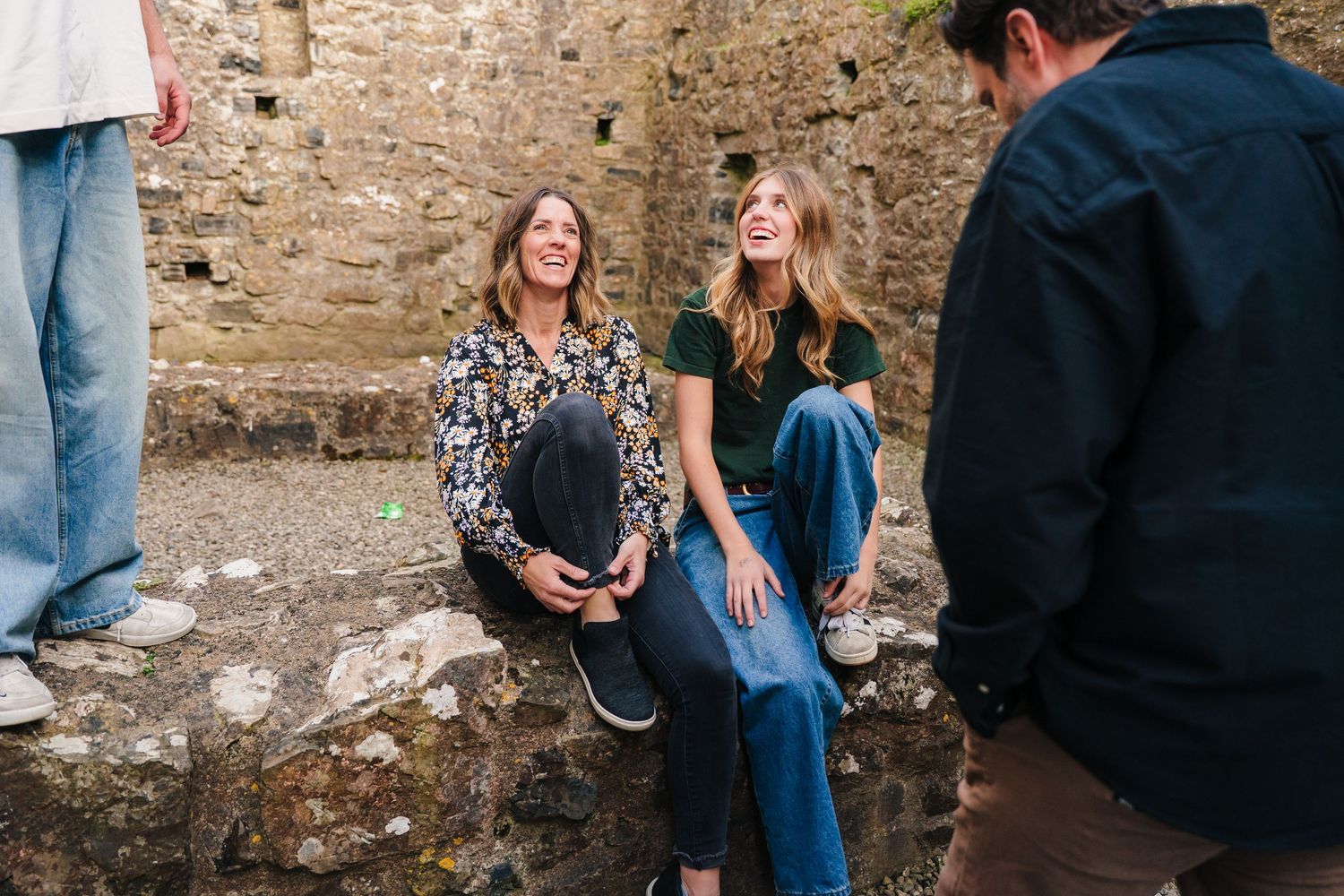 Five friends laughing and having fun together while leaning against a rustic stone wall in a casual outdoor setting. Photographer Ireland du