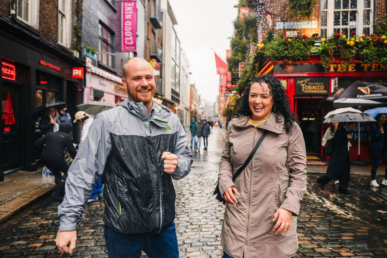 Proposal Dublin Photographer down a rainy cobblestone street in Dublin's Temple Bar district with colorful storefronts and wet pavement.