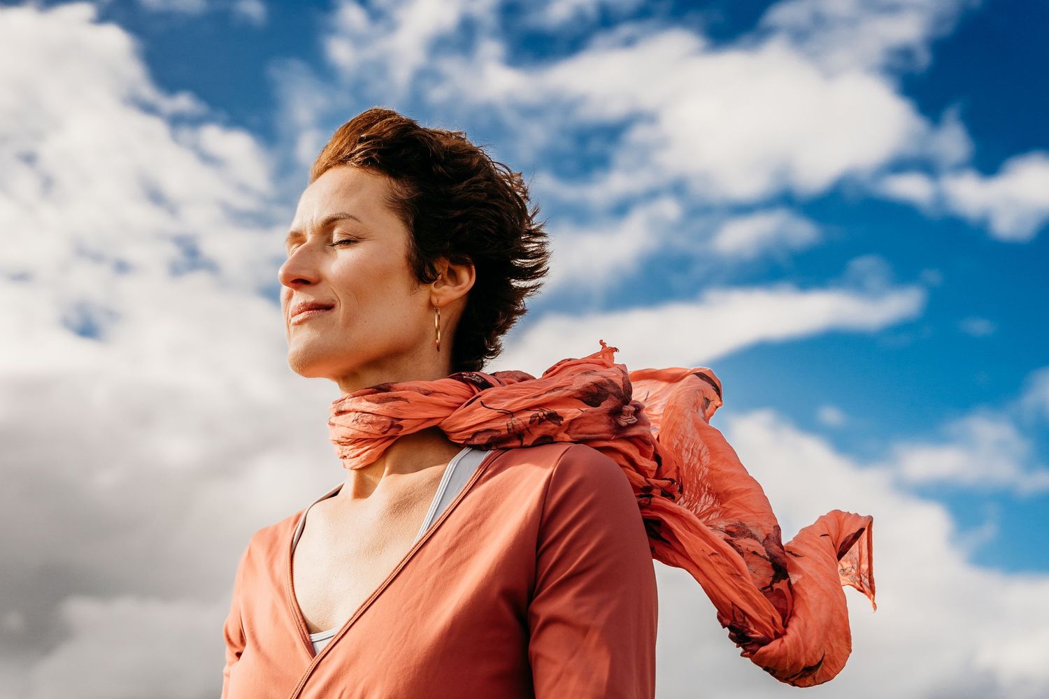 A salmon-colored dress flows in the wind against a bright blue sky dotted with white puffy clouds. Portrait PHOTOGRAPHER Dublin