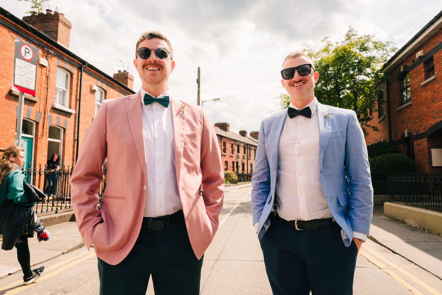 Wedding party members walk down sunny street wearing pastel and blue formal attire. Same sex wedding PHOTOGRAPHER Dublin