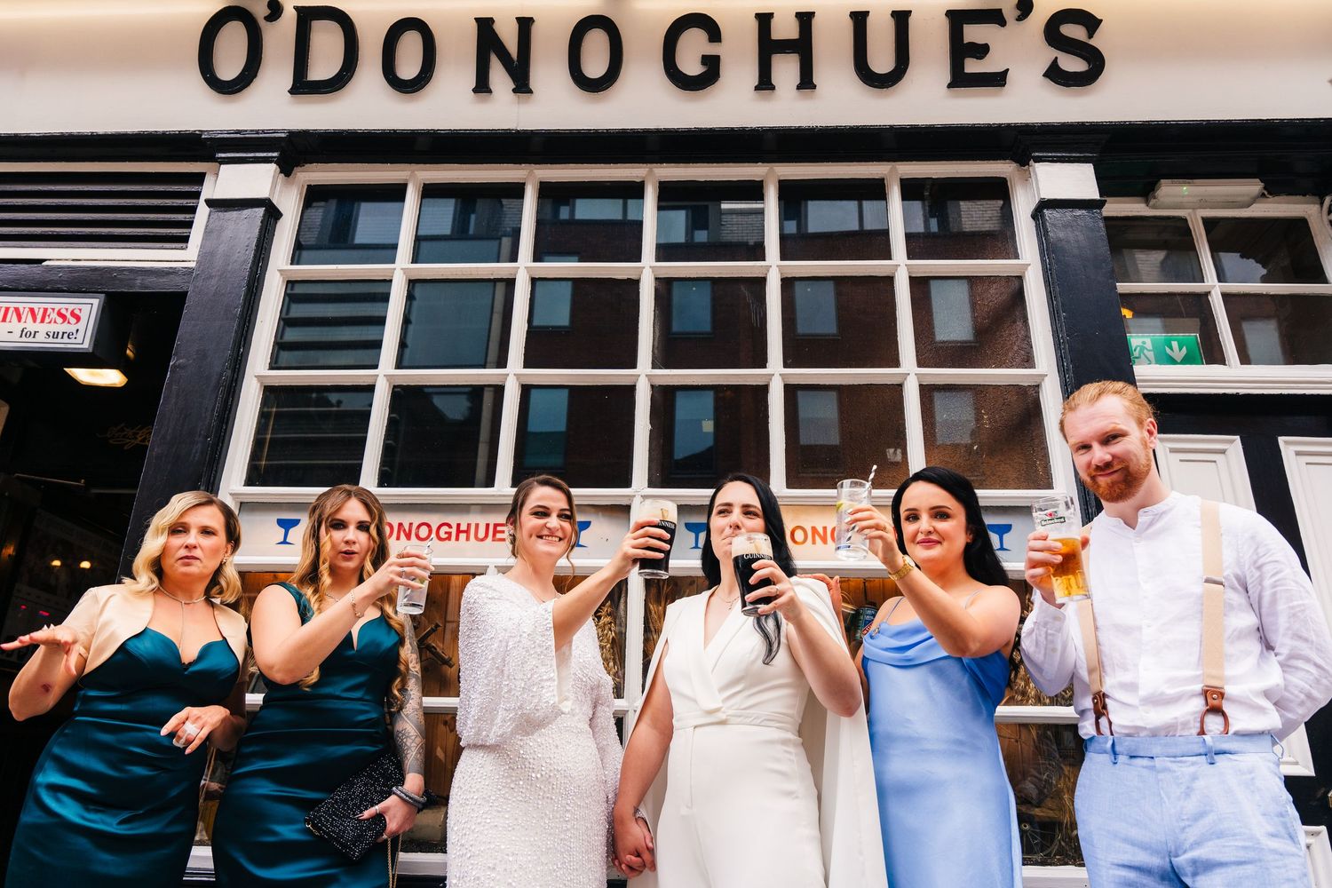 A group poses outside O'Donoghue's pub wearing formal attire and making celebratory gestures. House Dublin Wedding Photographer