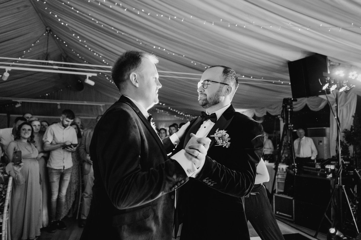 Black and white photo of wedding guests dancing and celebrating under a draped tent ceiling. LGBTQ Ashley Park Wedding Photographer