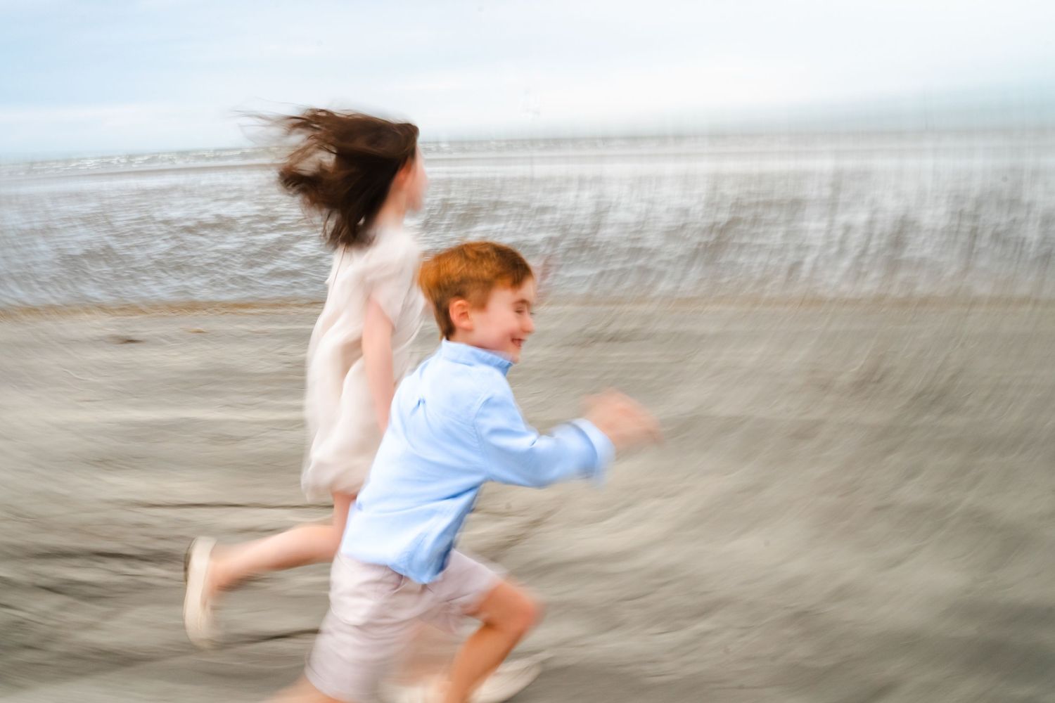 Couple walking and playing together on a sandy beach during golden hour at sunset.  Family photographer Dublin Ireland