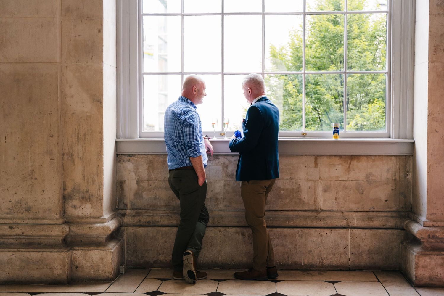Two people having intimate conversation by large window in historic building.