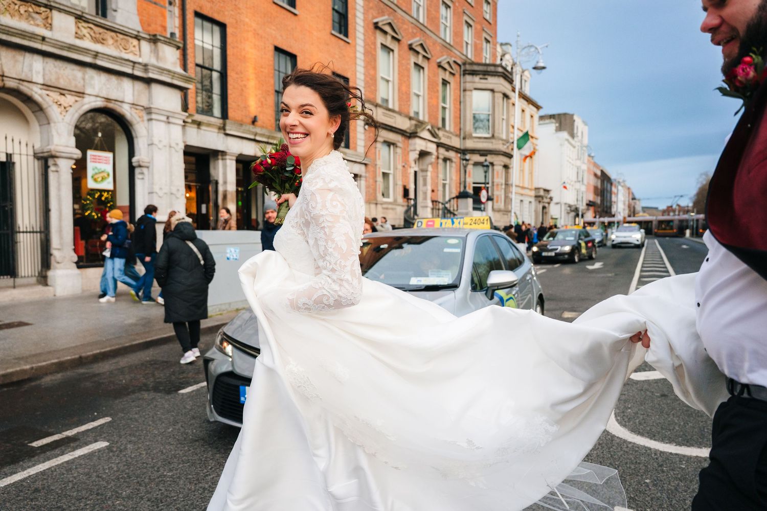 A bride in a flowing white wedding dress twirls joyfully on a city street lined with orange brick buildings. Stephens green club dublin Wedd
