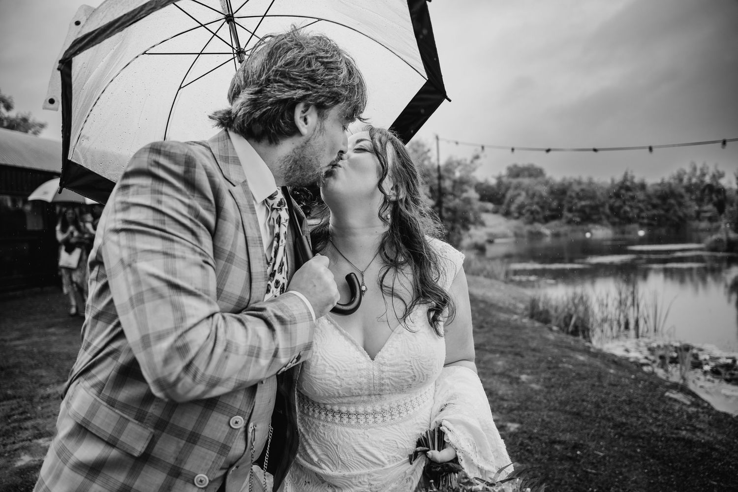 Black and white photo of couple sharing intimate moment under umbrella near water. Wedding photographer Dublin
