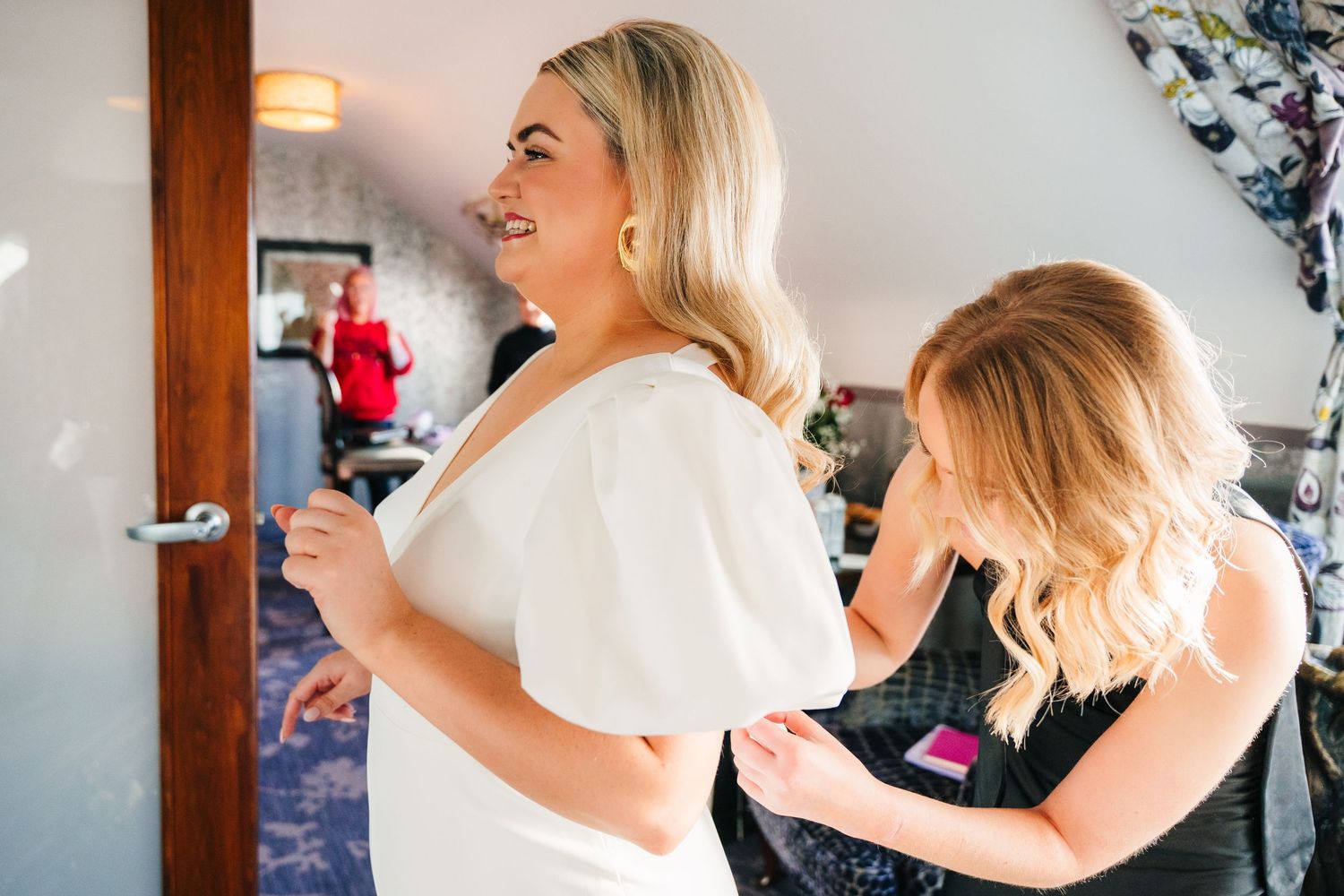 A person in a white dress has their hair styled while getting ready in a bridal suite. Wedding photographer dublin