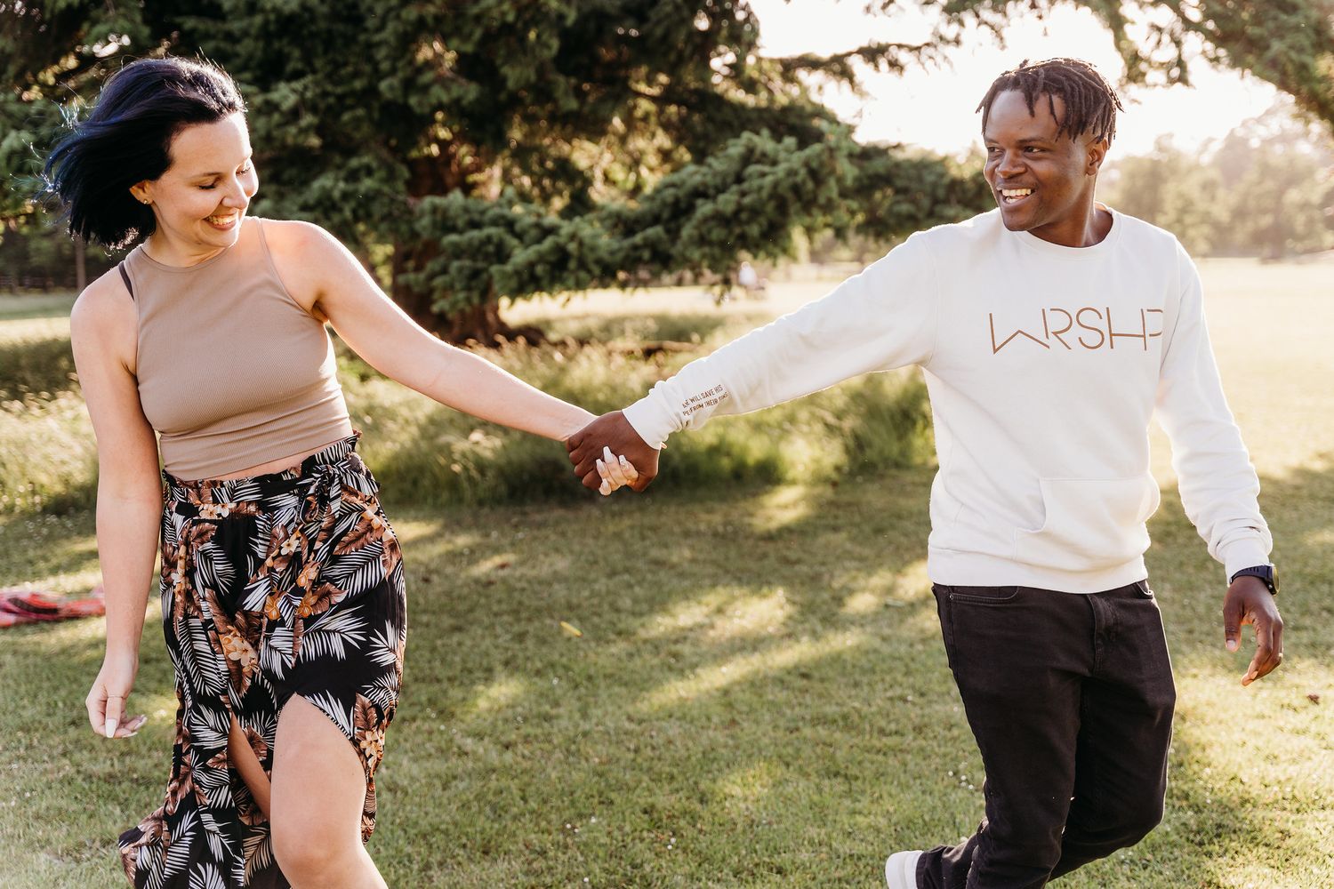 Two people holding hands and dancing joyfully together on a grassy lawn during a sunny afternoon. PHOTOGRAPHER Dublin ireland