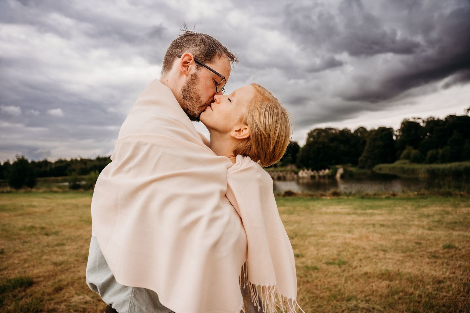 A couple embraces in a romantic kiss against moody storm clouds in an open field. PHOTOGRAPHER Dublin ireland