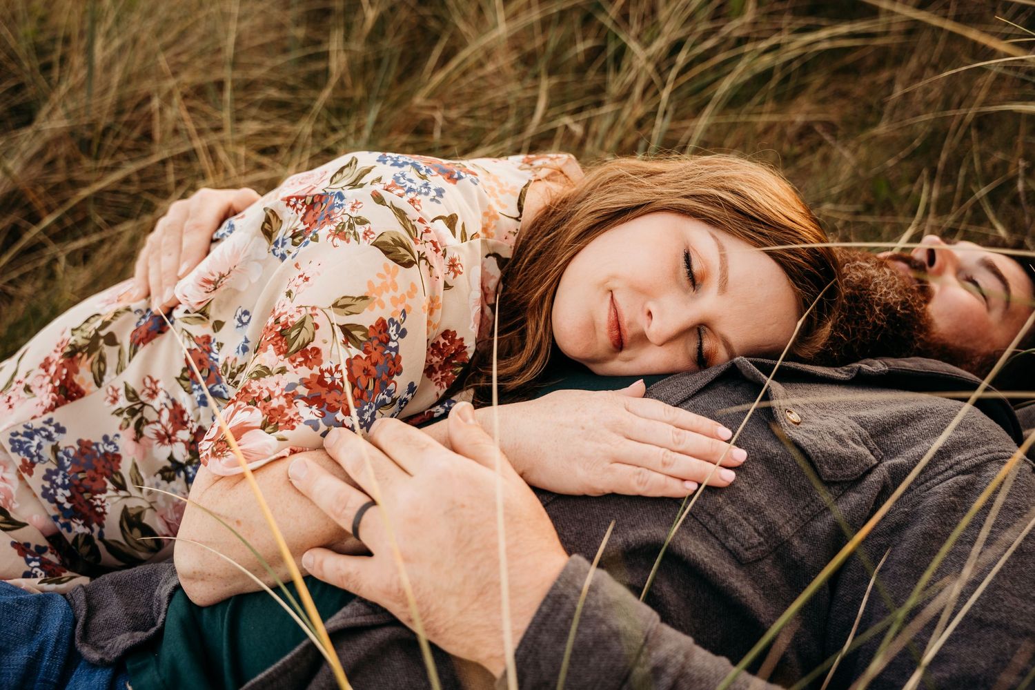 A woman lying in tall grass wearing a floral dress at sunset creates a romantic and dreamy outdoor portrait. PHOTOGRAPHER Dublin ireland