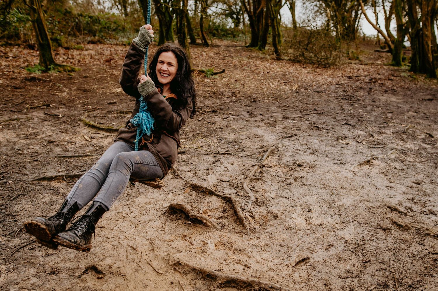 Adventurous hiker enjoys swinging from a rope swing on a muddy forest trail with autumn trees in the background.