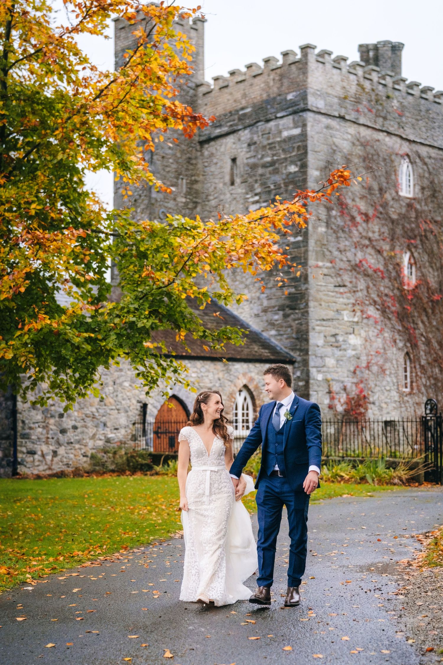 Wedding party walking along stone castle walls surrounded by vibrant autumn foliage.