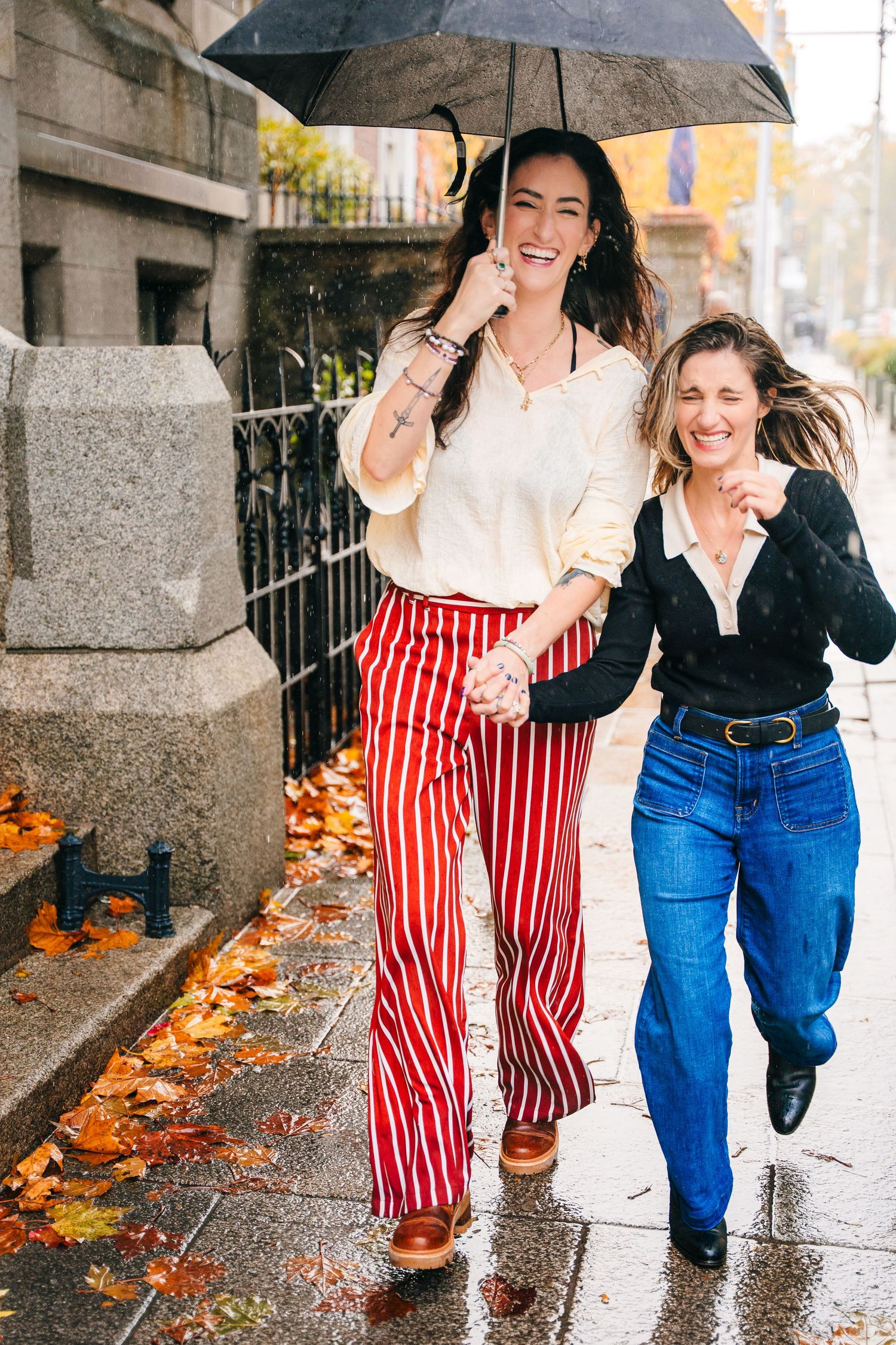Friends sharing umbrellas and laughing together while walking in the rain among fallen autumn leaves. professional headshots dublin photogra
