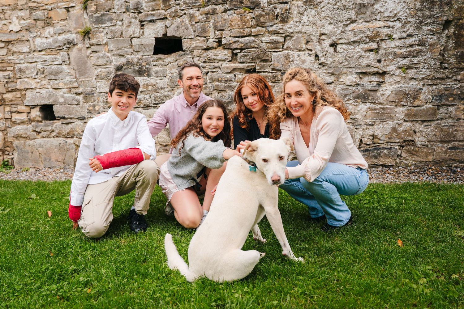 Family and pet relaxing together on grass near historic stone wall. BEctive abbey family photographer dublin