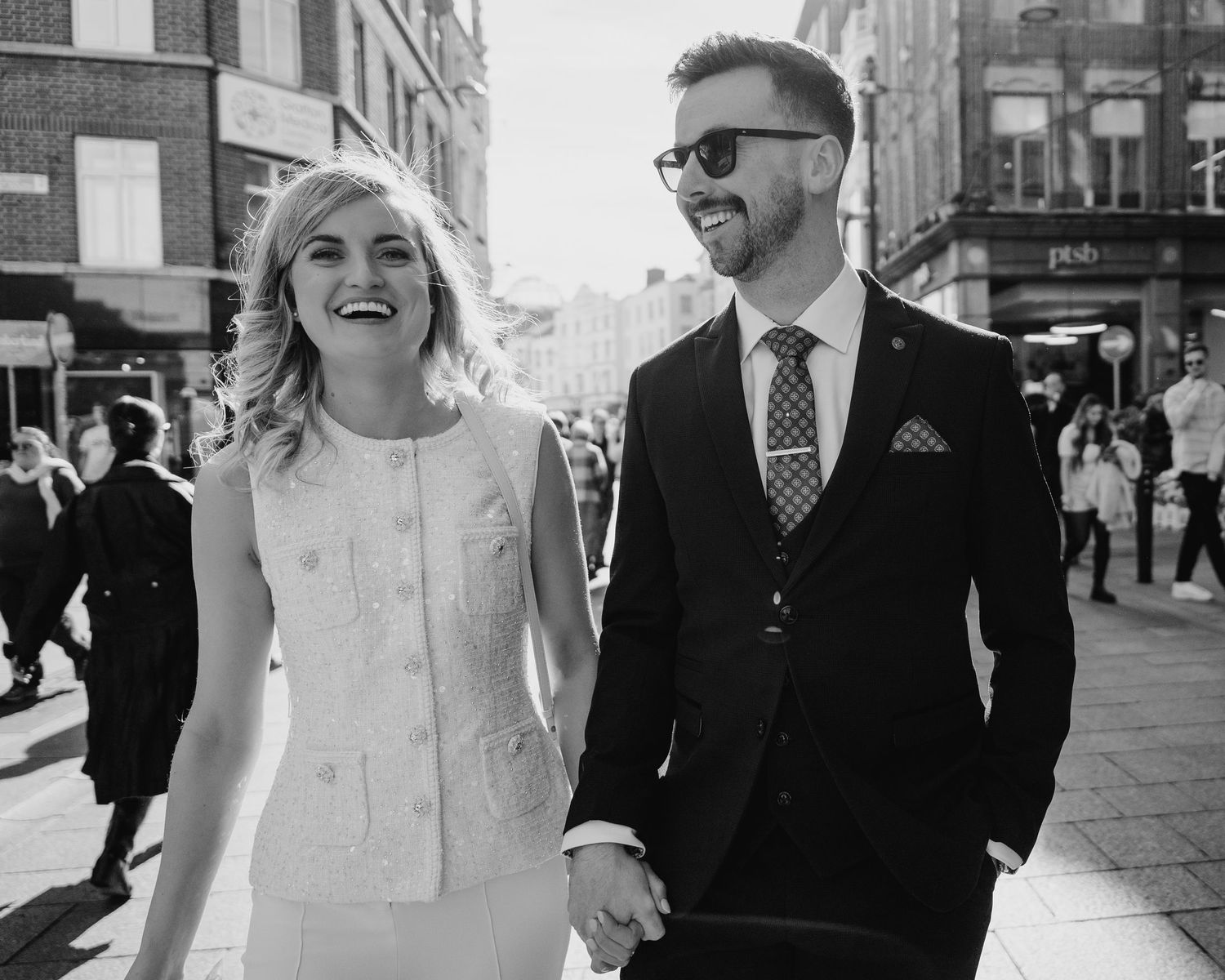 A couple walks together on a city street in black and white, with the person in a white dress smiling joyfully. City Hall Dublin wedding pho