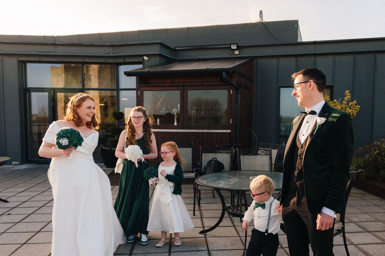 A group stands on a rooftop patio by a modern black building during a formal event.  Wedding PHOTOGRAPHER Trim Castle