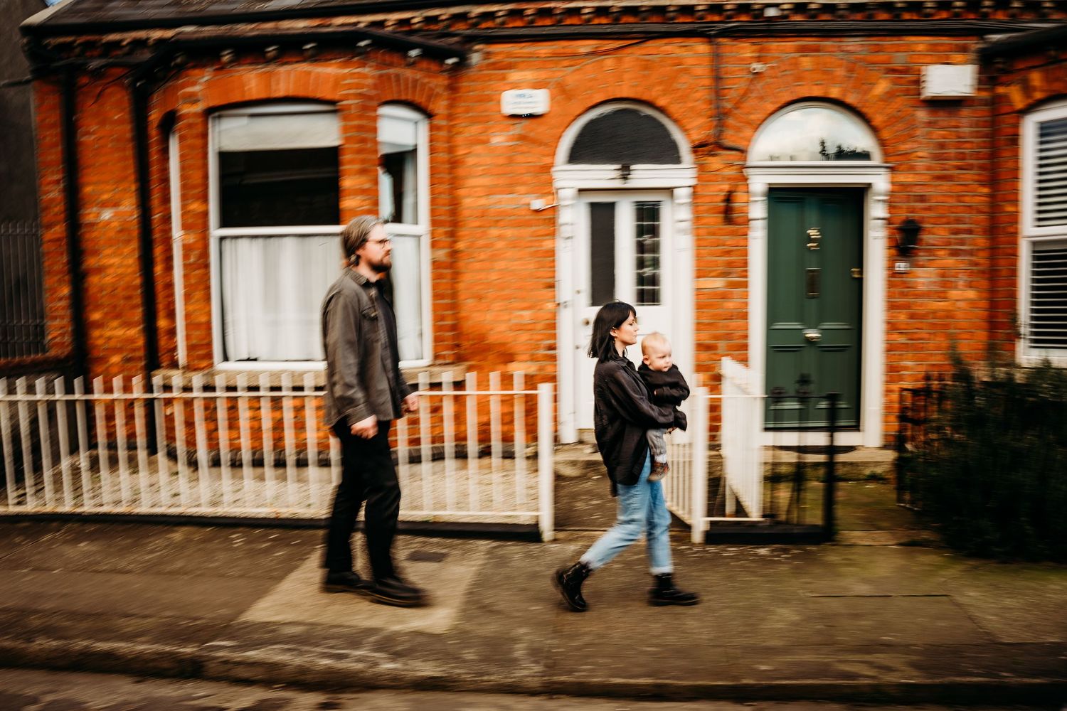 Two people walking past a classic red brick building with white trim and a dark green door in an urban setting.  Family PHOTOGRAPHER Dublin