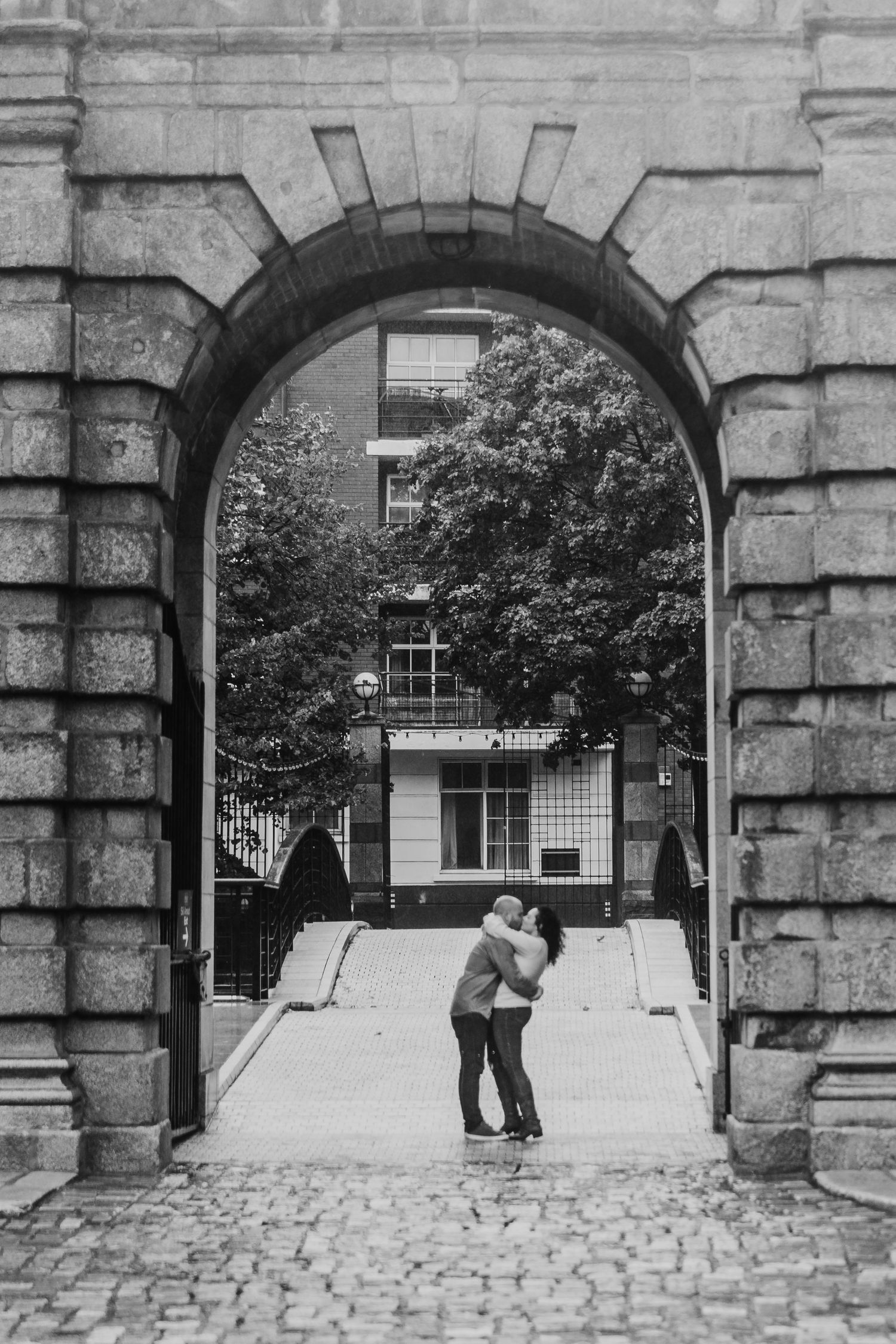 A sequence of playful moments captured through stone archways on a historic cobblestone courtyard. Proposal Dublin Photographer