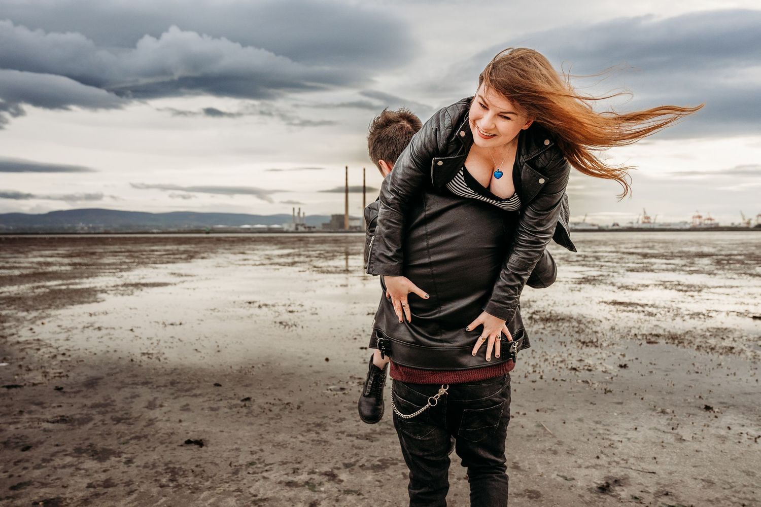 Person with wind-blown hair stands on beach against dramatic stormy sky. engagement PHOTOGRAPHER Dublin