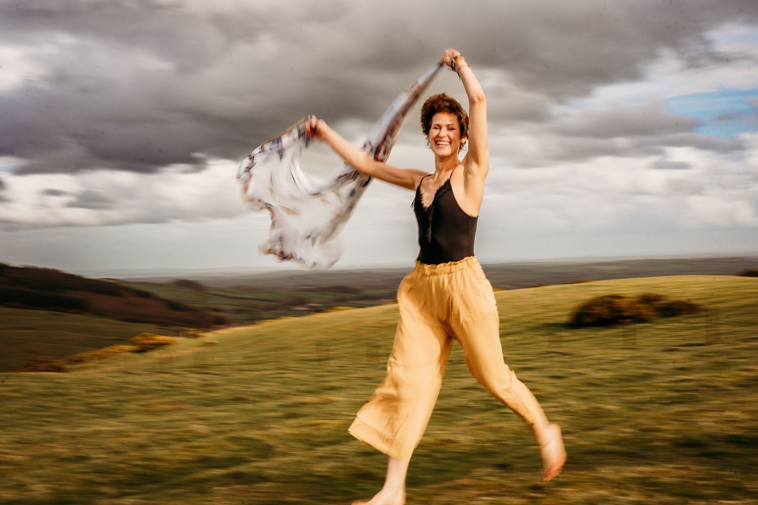 Dancer twirls with white fabric against dramatic sky over rolling green hills at sunset. Portrait PHOTOGRAPHER Dublin