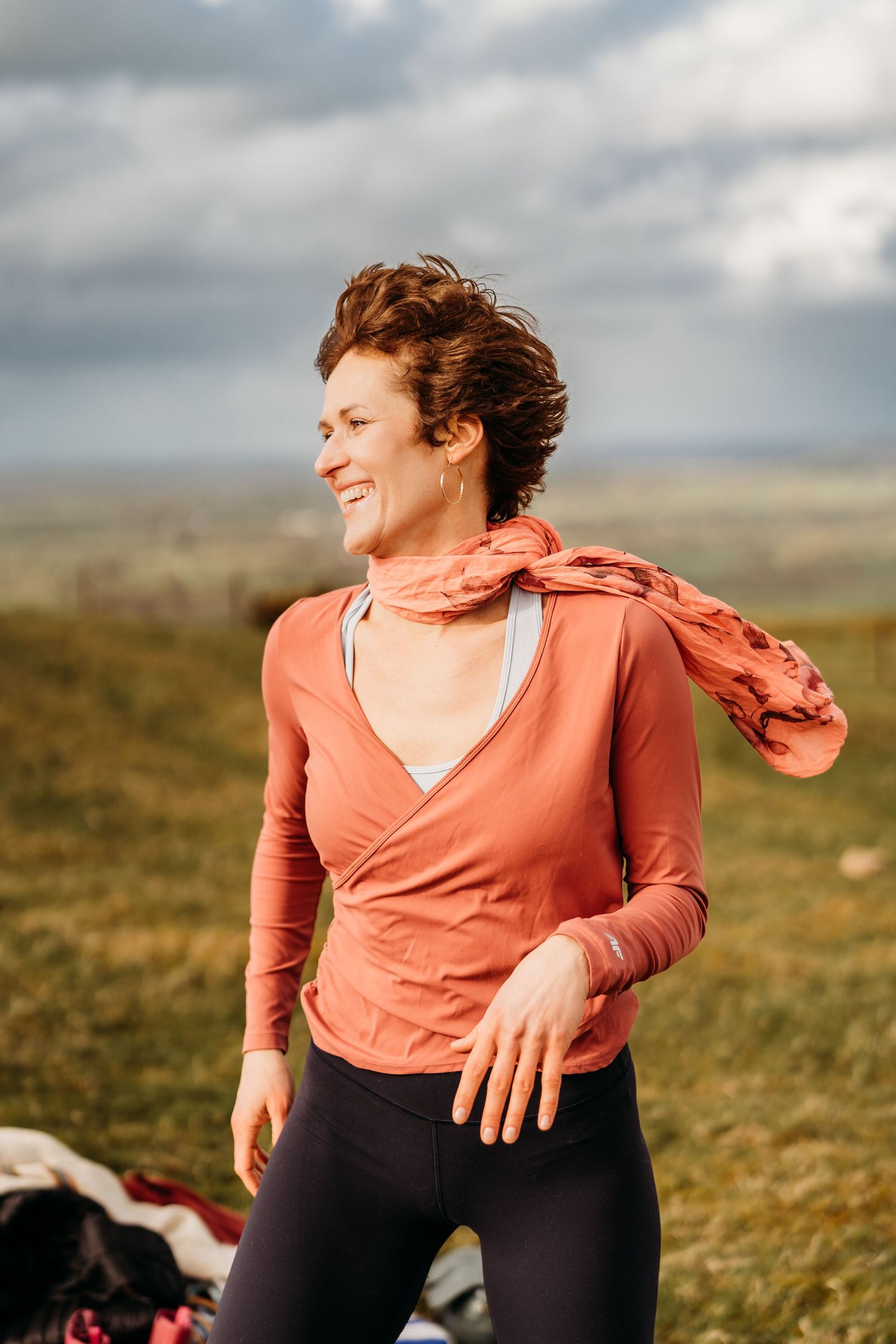 Person in a coral wrap top and black leggings smiles while enjoying a sunny day outdoors in a grassy field. Portrait PHOTOGRAPHER Dublin
