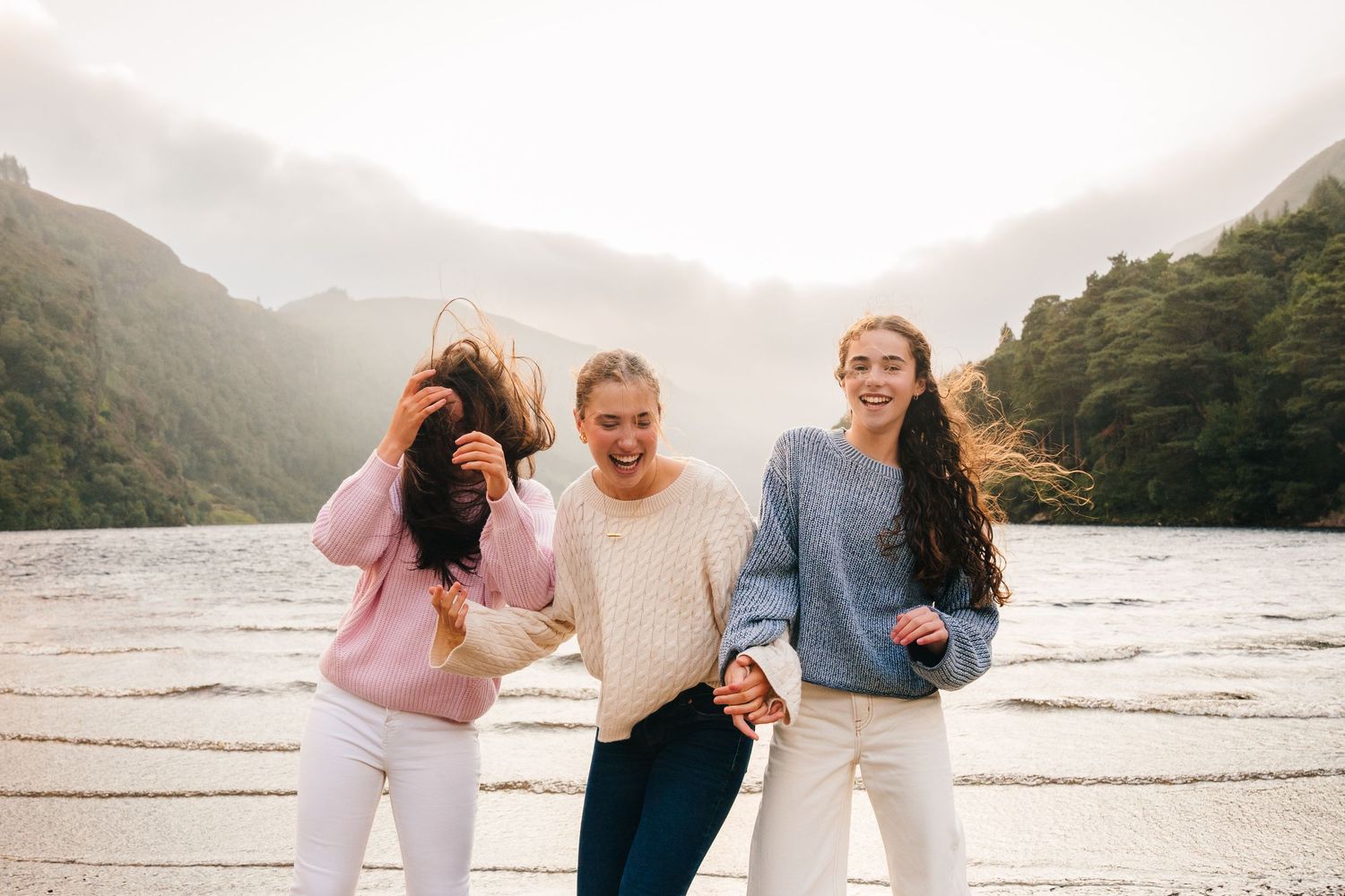 Family photographer Ireland Dublin Three friends enjoying a fun moment together at a misty mountain lake.