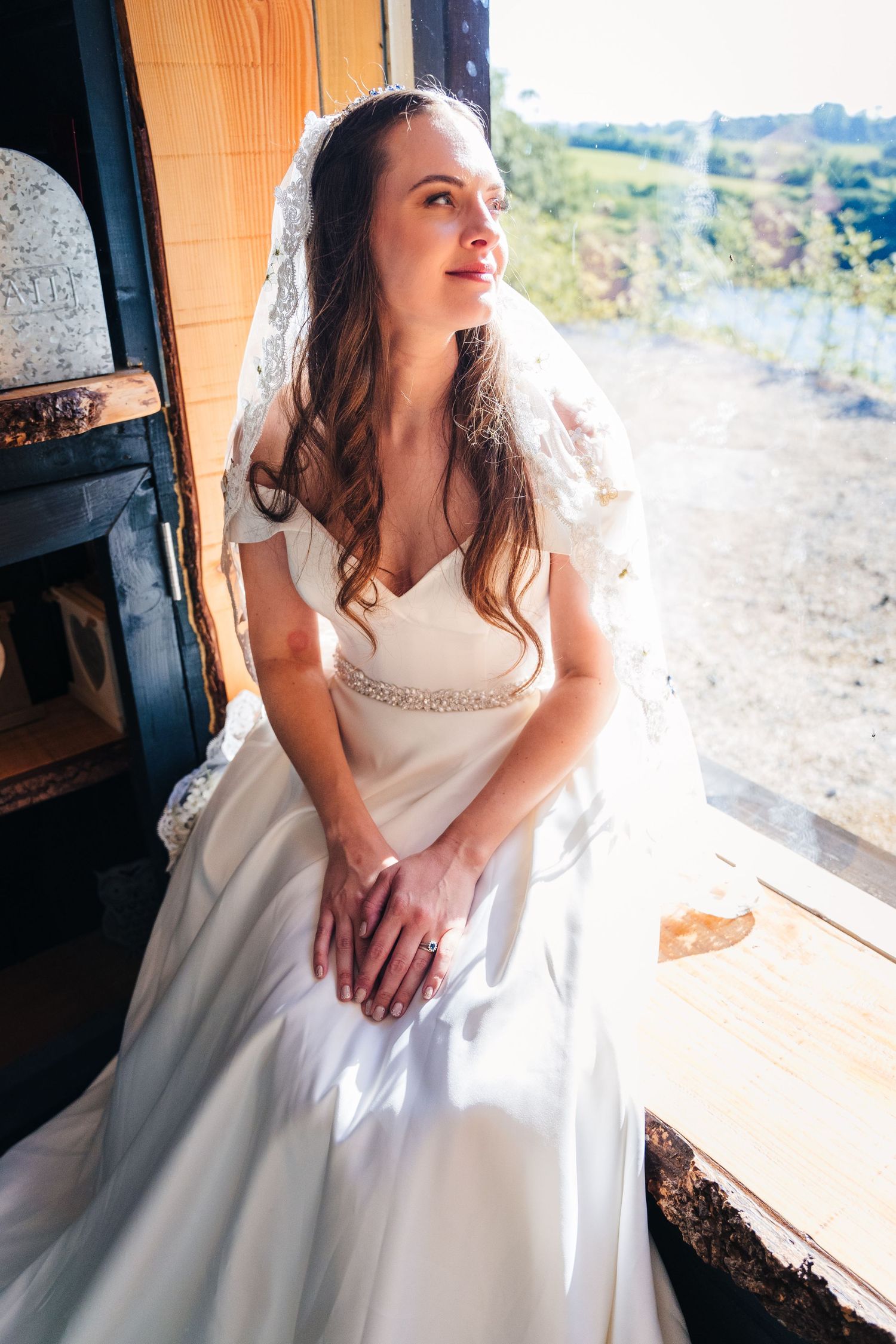 Poulaphouca Wedding photographer wicklow  A bride in an elegant white gown sits thoughtfully by a window with natural sunlight streaming in.
